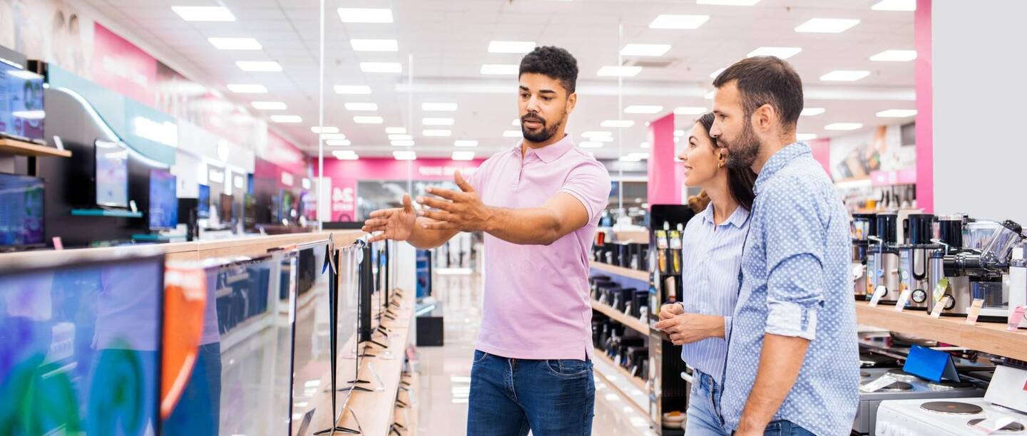 Una pareja en una tienda de electrónica es aconsejada por un vendedor